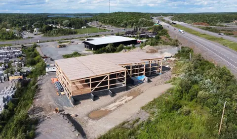 Aerial photo of the new timber-framed building under construction beside the highway, with the existing building beyond