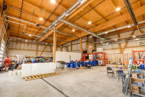 Warehouse interior under an exposed glulam roof structure, with equipment and storage racks