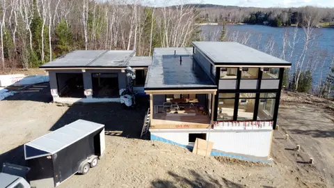 Aerial view of the modular cottage with a glazed corner and a lake behind