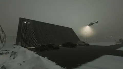 Night rendering of the angular hangar in snow as a helicopter lands