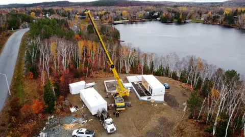 A crane setting a prefabricated module on the foundations beside the lake in autumn