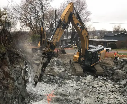 Excavator breaking bedrock on the lot at the start of construction