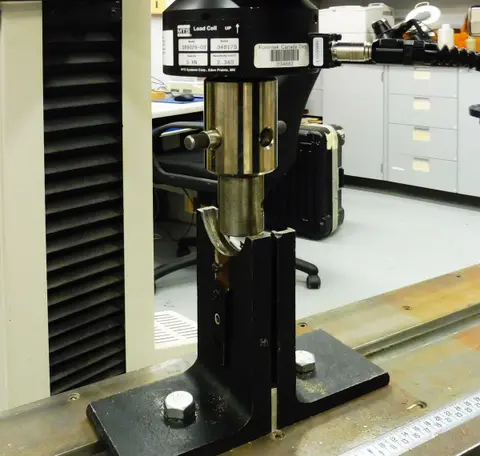 A folded paper sample under test in a materials testing machine