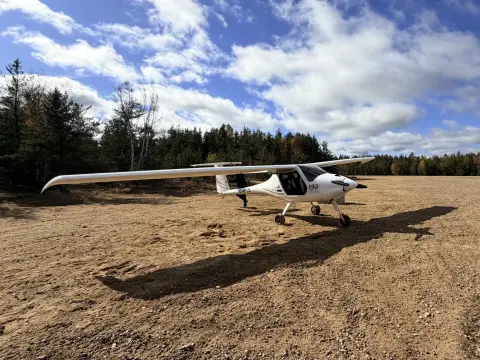 DAO's white Pipistrel Virus, registration C-IPYS, parked on an unpaved gravel airstrip beside a pine forest